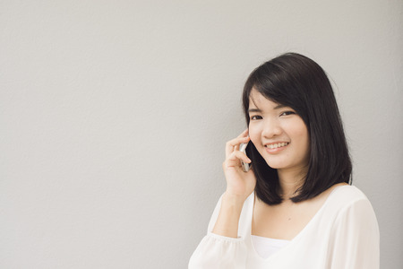 Beautiful asian young woman talking on Mobile Phone, over concrete wallの写真素材