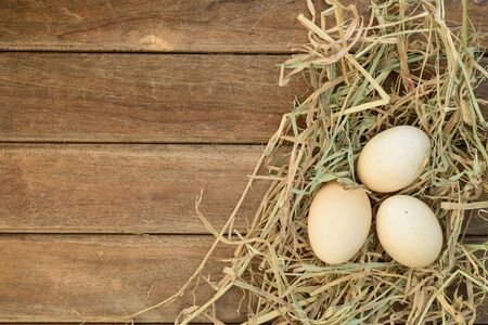 Egg in hay nest on old wooden table background, top viewの写真素材