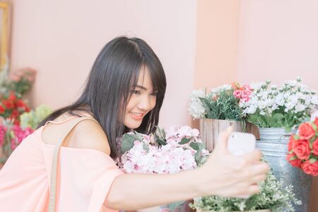 Technology internet and happiness concept. Woman content girl taking self picture selfie with smartphone camera while walking outdoors with flower in autumn park. Vintage filtered image.の写真素材
