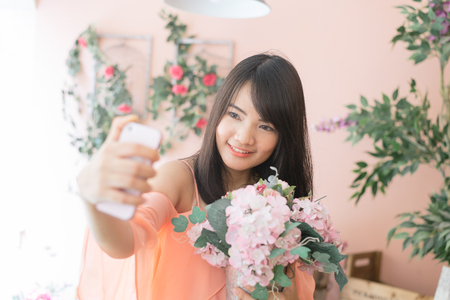 Technology internet and happiness concept. Woman content girl taking self picture selfie with smartphone camera while walking outdoors with flower in autumn park. Vintage filtered image.の写真素材