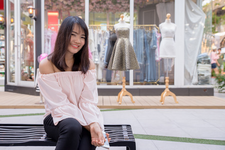 Charming young woman in white shirt reads or texts message to mobile phone, against old grunge houses in old city.の写真素材