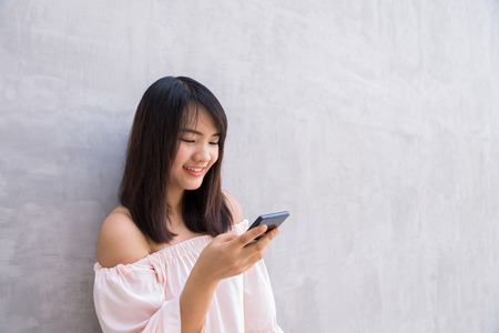 beautiful asian woman using cellphone, over concrete wallの写真素材