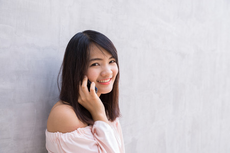 Beautiful asian young woman talking on Mobile Phone, over concrete wallの写真素材