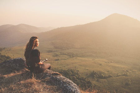 Hipster young girl with backpack enjoying sunset on peak of foggy mountain. Tourist traveler on background view mockup. Hiker looking sunlight in trip in Thailand country. Vintage filtered image.のeditorial素材
