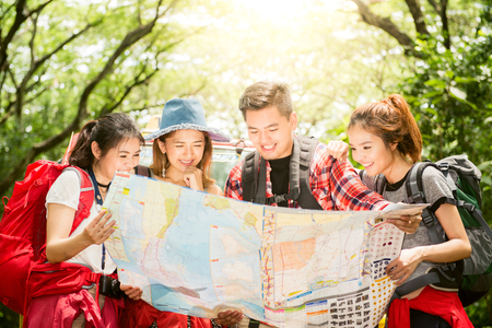 Hiking - hikers looking at map. Couple or friends navigating together smiling happy during camping travel hike outdoors in forest. Young mixed race Asian woman and man.の写真素材