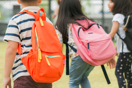 Three pupils of primary school go hand in hand. Boy and girl with school bags behind the back. Beginning of school lessons. Warm day of fall. Back to school. Little first graders.の写真素材