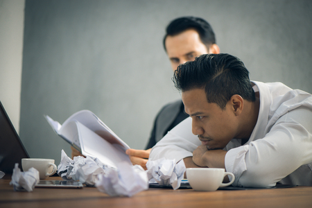 Worried businessman in dark suit sitting at office desk full with books and papers being overloaded with work. Vintage effect style pictures.の写真素材