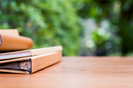 Books on a wooden desk at the in front of house with blurred garden view textured background.