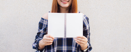 Beautiful young asian woman hiding behind a blank mock up book on concrete wall background. Vintage effect style pictures. Panoramic banner.の写真素材