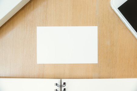 Closeup top view photo showing blank white business card and using modern laptop and mobile phone on wood table blurred background. Mockup ready for private information. Horizontal mock up.の写真素材