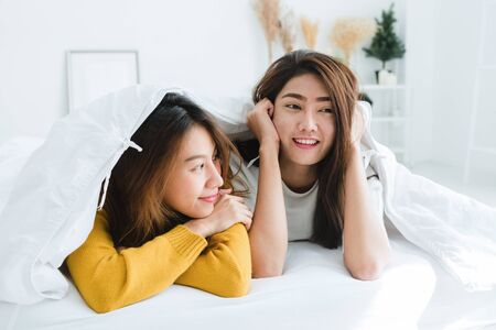 Top view of beautiful young asian women lesbian happy couple showing surprise and looking at camera while lying in bed under blanket. Funny women after wake up. Lesbian couple together indoors conceptの写真素材