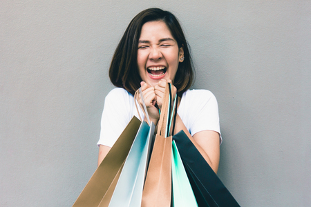 Young happy summer shopping asian woman with shopping bags on grey background at copy spaceの写真素材