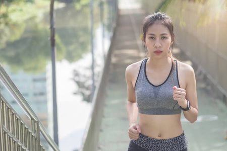 Young asian woman running on sidewalk in morning. Health conscious concept with copy space. Young...