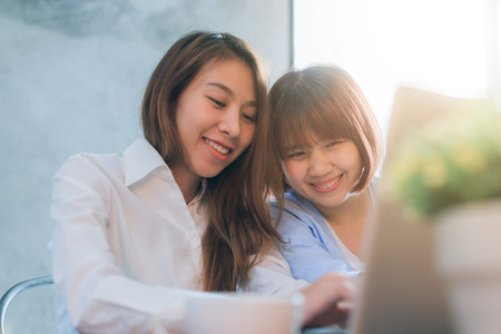 Two young business women sitting at table in cafe. Asian women using laptop and cup of coffee. Freelancer working in coffee shop. Working outside office lifestyle. One-on-one meeting.の写真素材