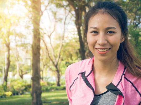 Close up of a happy young asian woman warming up her body by stretching her body before morning excercise and yoga in the park cover with nature and warm light morning. Outdoor excercise concept.の写真素材