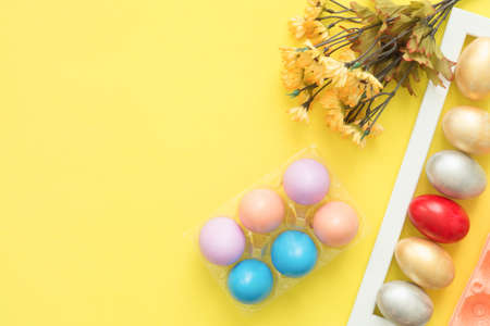Flat lay top view colorful easter egg painted in pastel colors composition and spring flowers on yellow pastel color background. Easter day background top view with copy space.の写真素材