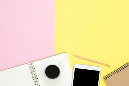 Office desk working space - Flat lay top view photo of working space with blank mock up tablet, coffee cup and notebook on pastel background. Pastel pink yellow color copy space working desk concept.の写真素材