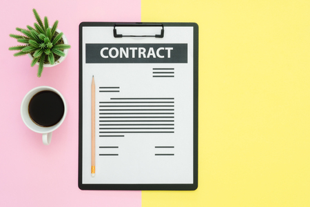 Flat lay design of office desk working space  - Top view of a contract document and coffee cup decorated with small cactus on pink yellow pastel color with copy space. Pastel working space background.の写真素材