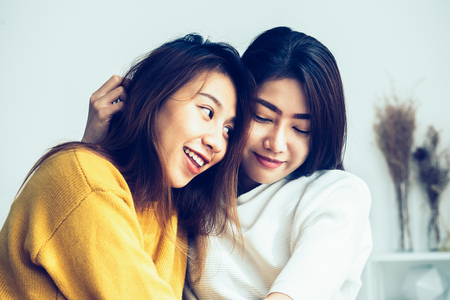Beautiful young asian women LGBT lesbian happy couple sitting on bed hugging and smiling together in bedroom at home. LGBT lesbian couple together indoors concept. Spending nice time at home.の写真素材