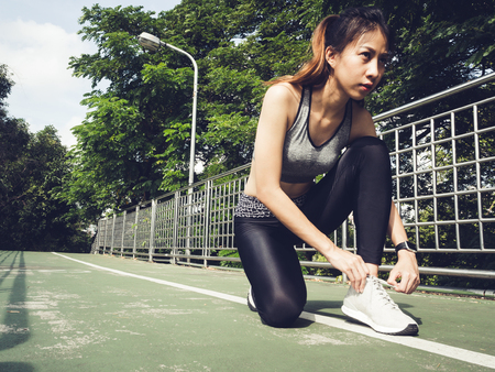 Close up of young woman lace up her shoe ready to workout on exercising in the park with warm light sunshine in morning. Young woman prepare for outdoor exercise in park. Outdoor exercise concept.の写真素材