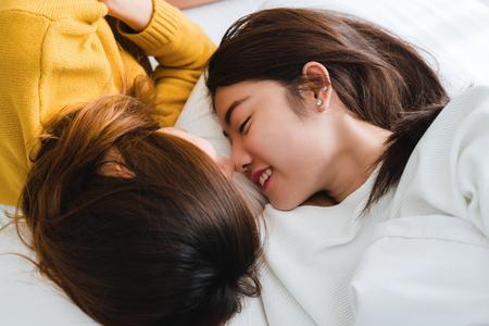 Beautiful young asian women LGBT lesbian happy couple hugging and smiling while lying together in bed under blanket at home. Funny women after wake up. LGBT lesbian couple together indoors concept.の写真素材