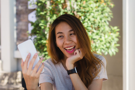 Attractive beautiful happy young Asian woman taking a selfie using a smart phone at cafe. Young Asian girl at restaurant taking self portrait.の写真素材