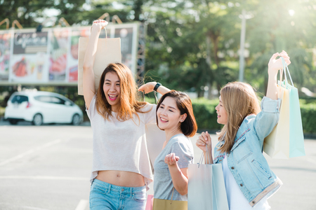 Group of young Asian Woman shopping in an outdoor market with shopping bags in their hands. Young women show what they got in shopping bag under warm sunlight. Group outdoor shopping concept.の写真素材