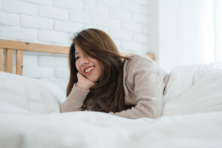 Portrait beautiful young Asian woman on bed at home in the morning. Cheerful Asian woman wearing a comfortable sweater and smiling on her bed. Relaxing room. lifestyle asia woman at home concept.の写真素材