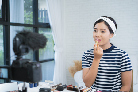 Beauty blogger present beauty cosmetics while sitting in front camera for recording video. Beautiful woman use lipstick while review make up tutorial broadcast live video to social network by internet.の写真素材