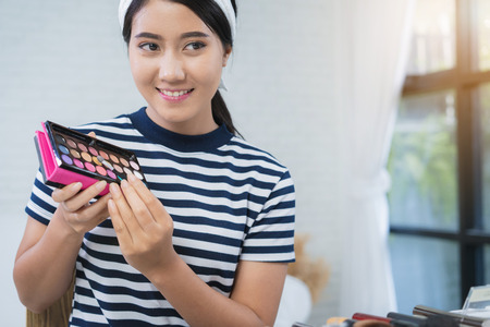 Beauty blogger present beauty cosmetics while sitting in front camera for recording video. Beautiful woman use brush while review make up tutorial broadcast live video to social network by internet.の写真素材