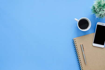 Office desk working space - Flat lay top view mockup photo of working space with tablet, phone, coffee cup and notebook on blue pastel background. Pastel blue color copy space working desk concept.の写真素材