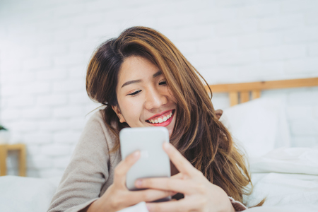 Happy Asian women are using smart phone on the bed in morning.の写真素材