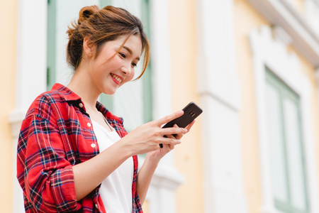Asian woman tourist backpacker smiling and using smartphone traveling alone holidays outdoors on city street in Bangkok - Thailand.の写真素材