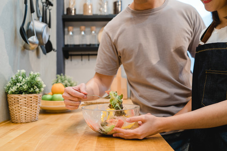 Beautiful happy asian couple are feeding each other in the kitchen.の写真素材