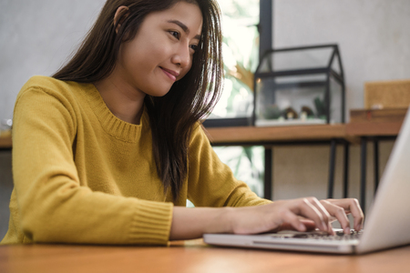 Young asian woman working with the laptop on a desk with her smile.の写真素材