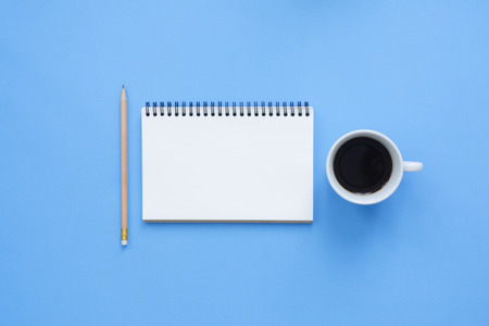 Office desk working space - Flat lay top view mockup of a working space with white blank notebook page, coffee cup on blue pastel background.の写真素材