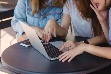 Group of beautiful smart business freelance Asian women in smart casual wear working together on laptop or computer while sitting on table in creative office or cafe.の写真素材