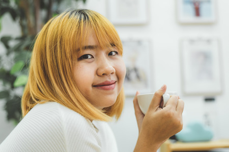 Attractive beautiful asian woman enjoying warm coffee in the kitchen at her home. Asian female wearing comfortable sweater holding a cup of coffee. lifestyle asia woman at home concept.の写真素材