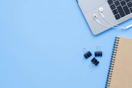 Office desk working space - Flat lay top view mockup photo of a working space with laptop, notebook and earphone on blue pastel background. Pastel blue color copy space working desk concept.の写真素材