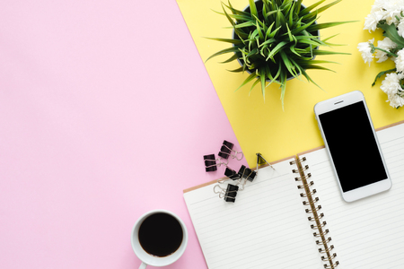Office desk working space - Flat lay top view of a working space with white blank notebook page, coffee cup and mock up phone on pastel background. Pastel pink yellow color background space concept.の写真素材