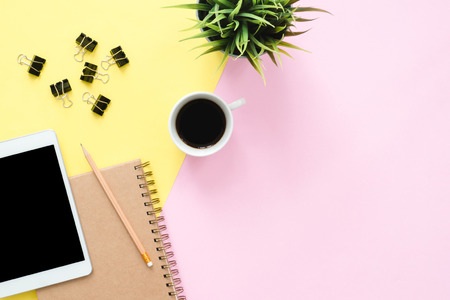 Office desk working space - Flat lay top view photo of working space with blank mock up tablet, coffee cup and notebook on pastel background. Pastel pink yellow color copy space working desk concept.の写真素材