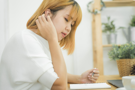Beautiful young smiling asian woman working on laptop while sitting in a living room at home. Asian business woman working in her home office. Enjoying time at home.の写真素材
