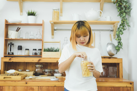 Asian woman holding and eating junk food snack and chips in her kitchen at home, female enjoy unhealthy food. Lifestyle women relax and enjoy junk food in kitchen at home concept.の写真素材