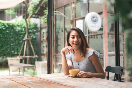 Cheerful asian young woman drinking warm coffee or tea enjoying it while sitting in cafe. Attractive happy asian woman holding a cup of coffee.の写真素材