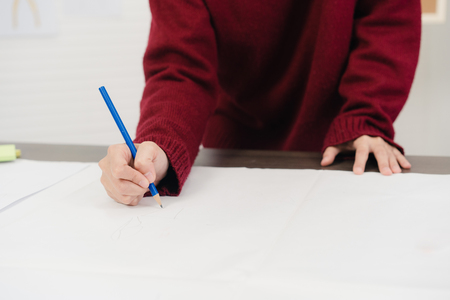 Professional beautiful Asian female fashion designer working with fabric sketches and drawing clothing design at the studio. Lifestyle women working concept.の写真素材