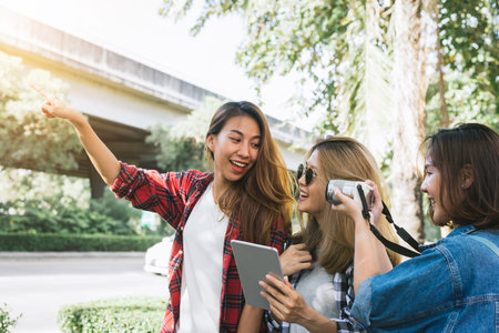 Group of Asian women using camera to make photo while traveling at park in urban city in Bangkok,...