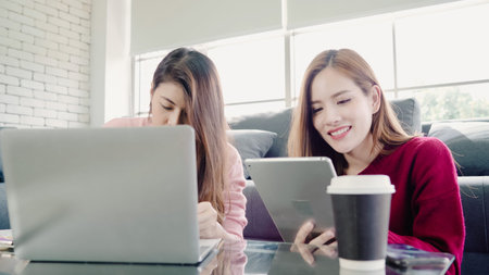 Lesbian Asian couple using laptop making budget in living room at home, sweet couple enjoy love...