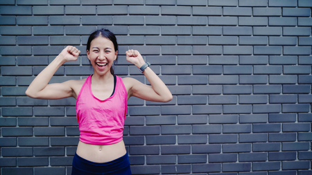 Healthy beautiful young Asian runner woman feeling happy smiling and looking to camera after running on street in urban city. Lifestyle fit and active women exercise in the city concept.の写真素材