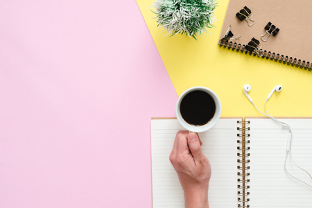 Creative flat lay photo of workspace desk. Top view office desk with notebooks, plant, coffee cup, earphone and copy space on pastel color background. Top view with copy space, flat lay photography.の写真素材