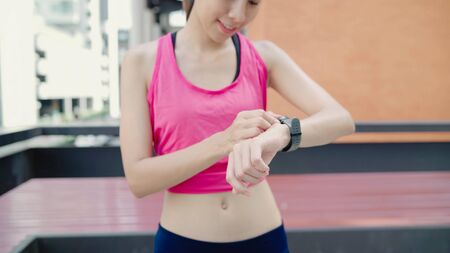 Healthy beautiful young Asian Athlete woman setting and checking progress looking heart rate monitor on smart watch while running in urban city. Lifestyle women exercise in the city concept.の写真素材